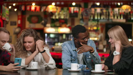 Tell-funny-stories-in-a-friends-company.-Multinational-men-and-woman-sitting-together-at-a-table-with-cups-of-coffee.